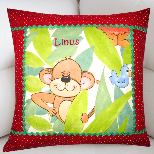 Handgefertigtes personalisiertes Kissen 40x40 cm mit niedlichem Affenmotiv, rotem gepunktetem Rand, grüner Zackenlitze und Namensbestickung „Linus“.